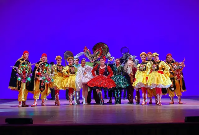 Elenco de Kahuira con trajes de diablada, caporal y figuras de La Tirana sobre un escenario iluminado de azul