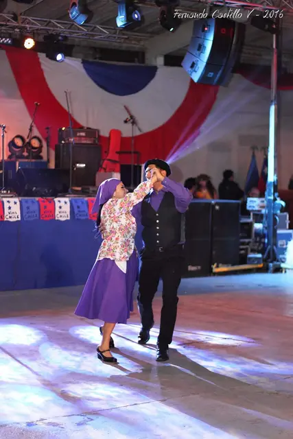 Pareja con vestuario chilote morado bailando sobre un escenario iluminado